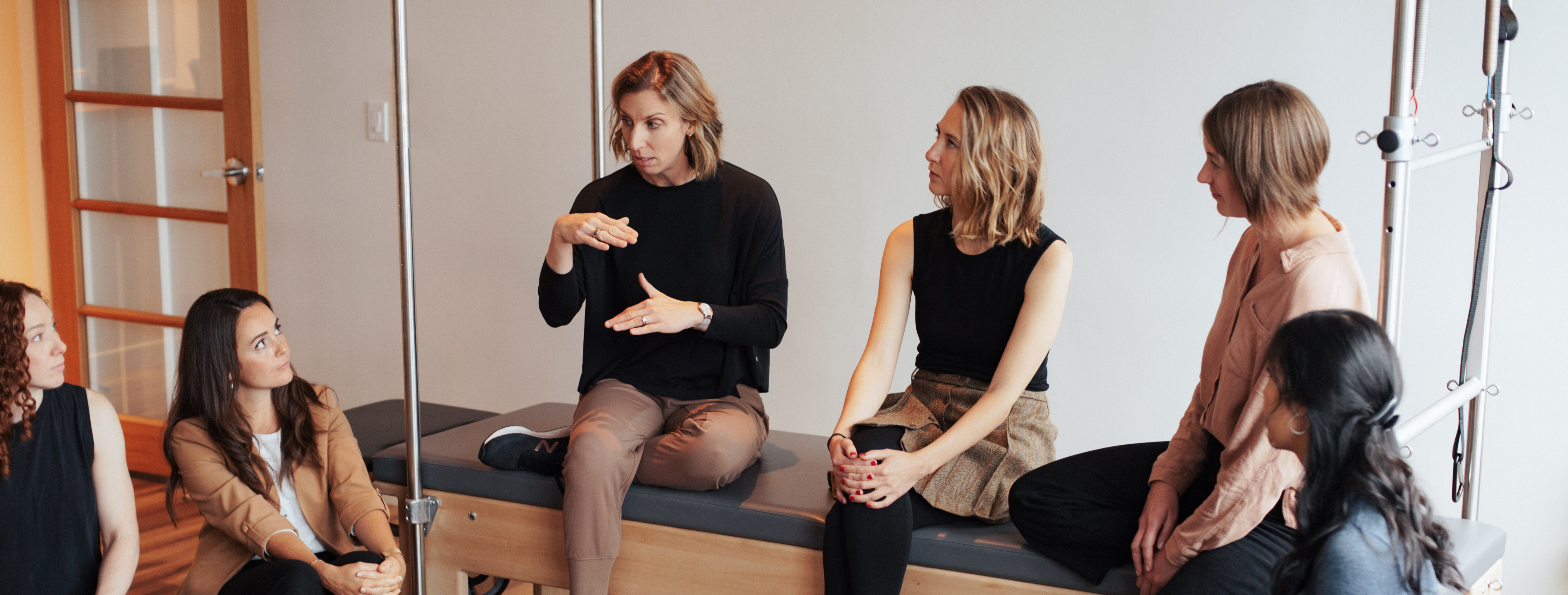 Team of dedicated pelvic physios discussing while sitting on a pilates reformer. 