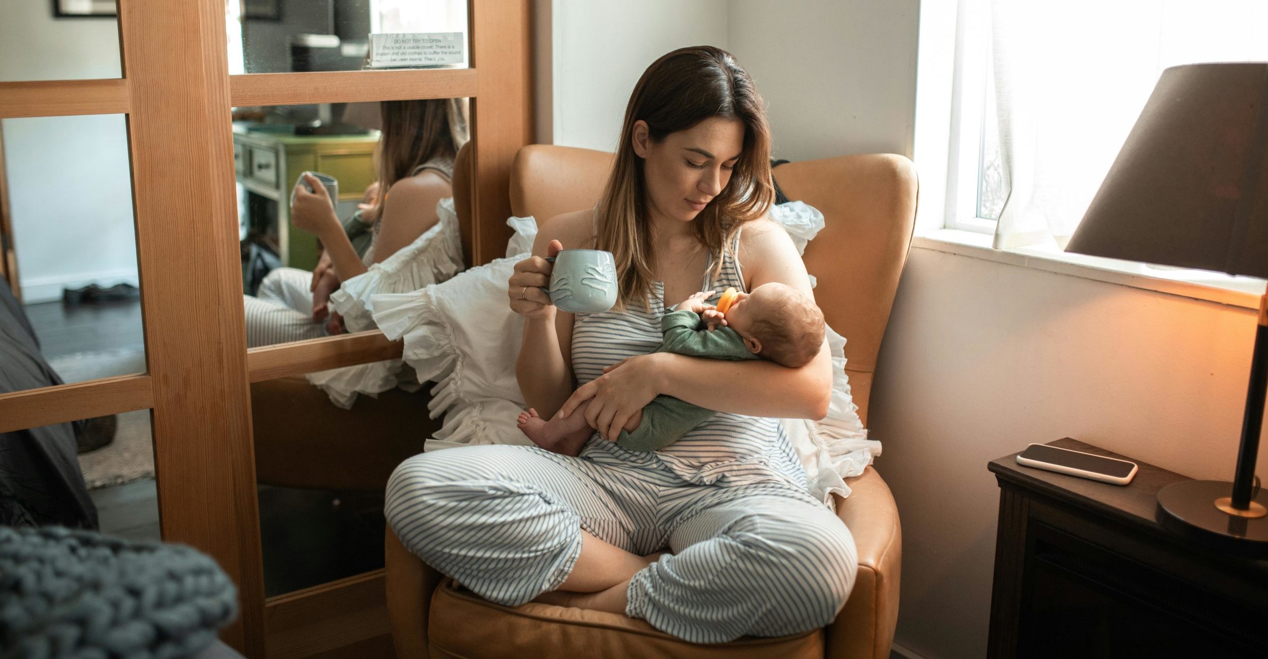 Person in pajamas holding a baby wiht a coffee cup in hand.