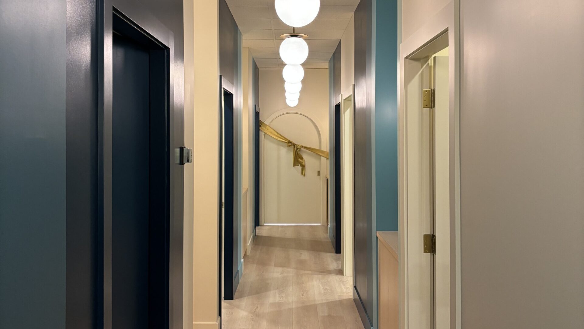 The new clinic's hallway. The walls are colour-blocked with varying shades of blue paint, and at the end of the hall a door is draped with a 'grand opening' style gold ribbon.