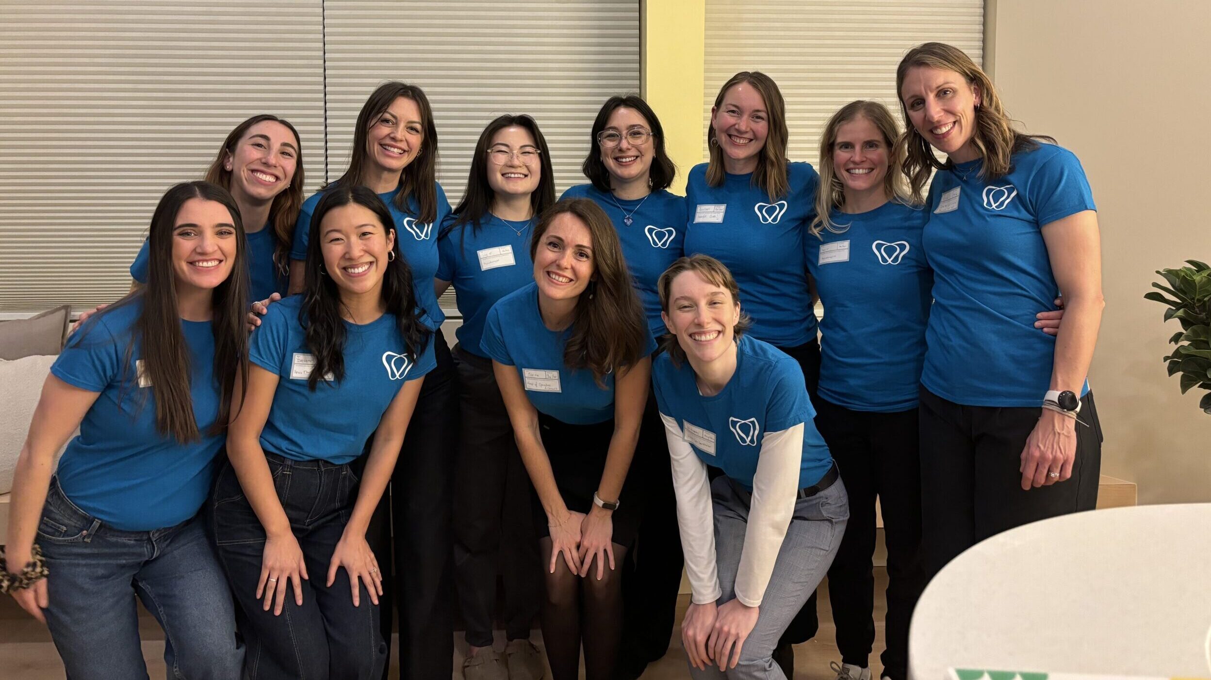 The Cheerful team are all stand arm-in-arm in the new clinic waiting room smiling. They are all wearing matching blue Cheerful Pelvis branded t-shirts.