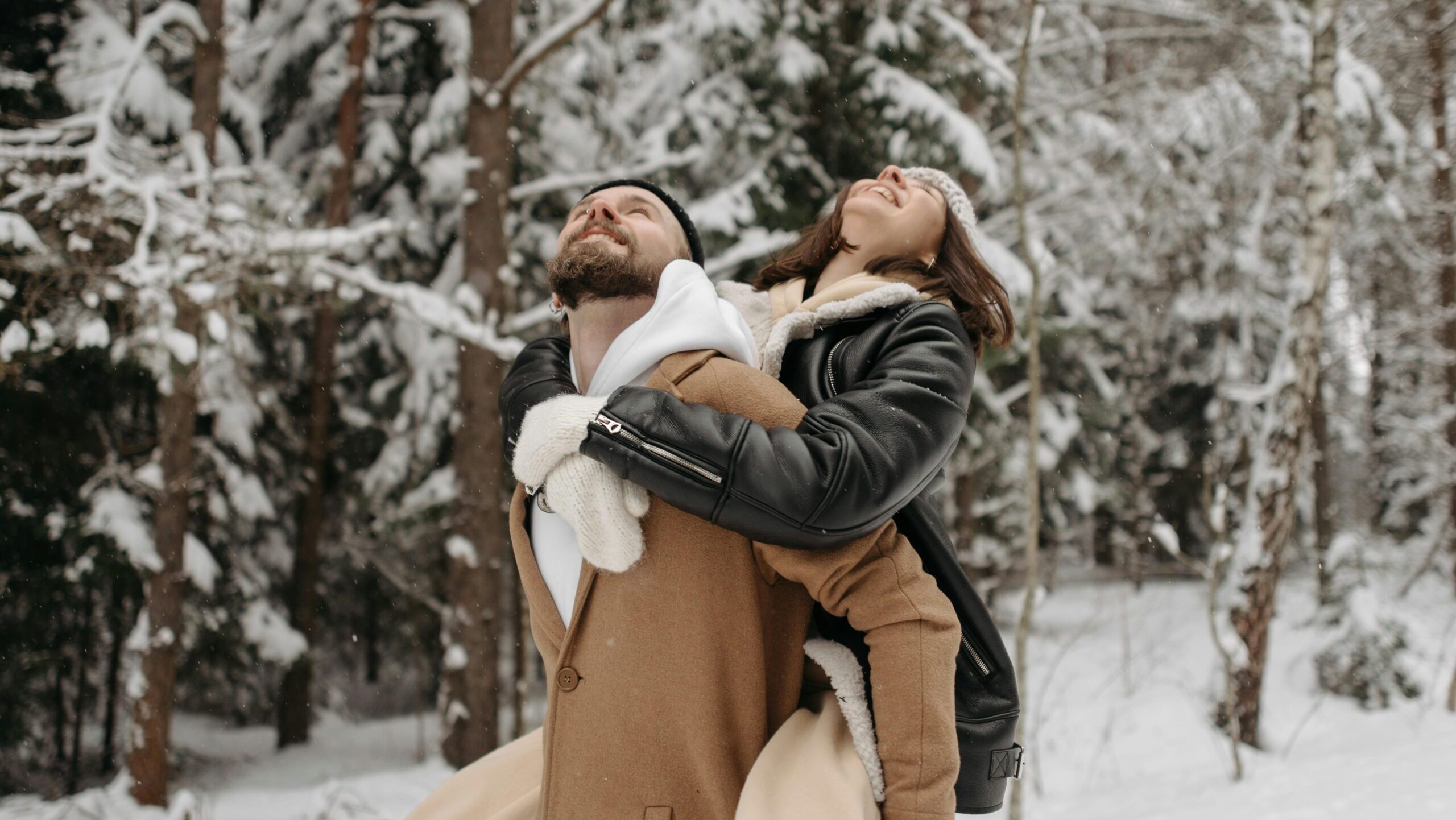 A person carrying another person on their back through a snowy forest.