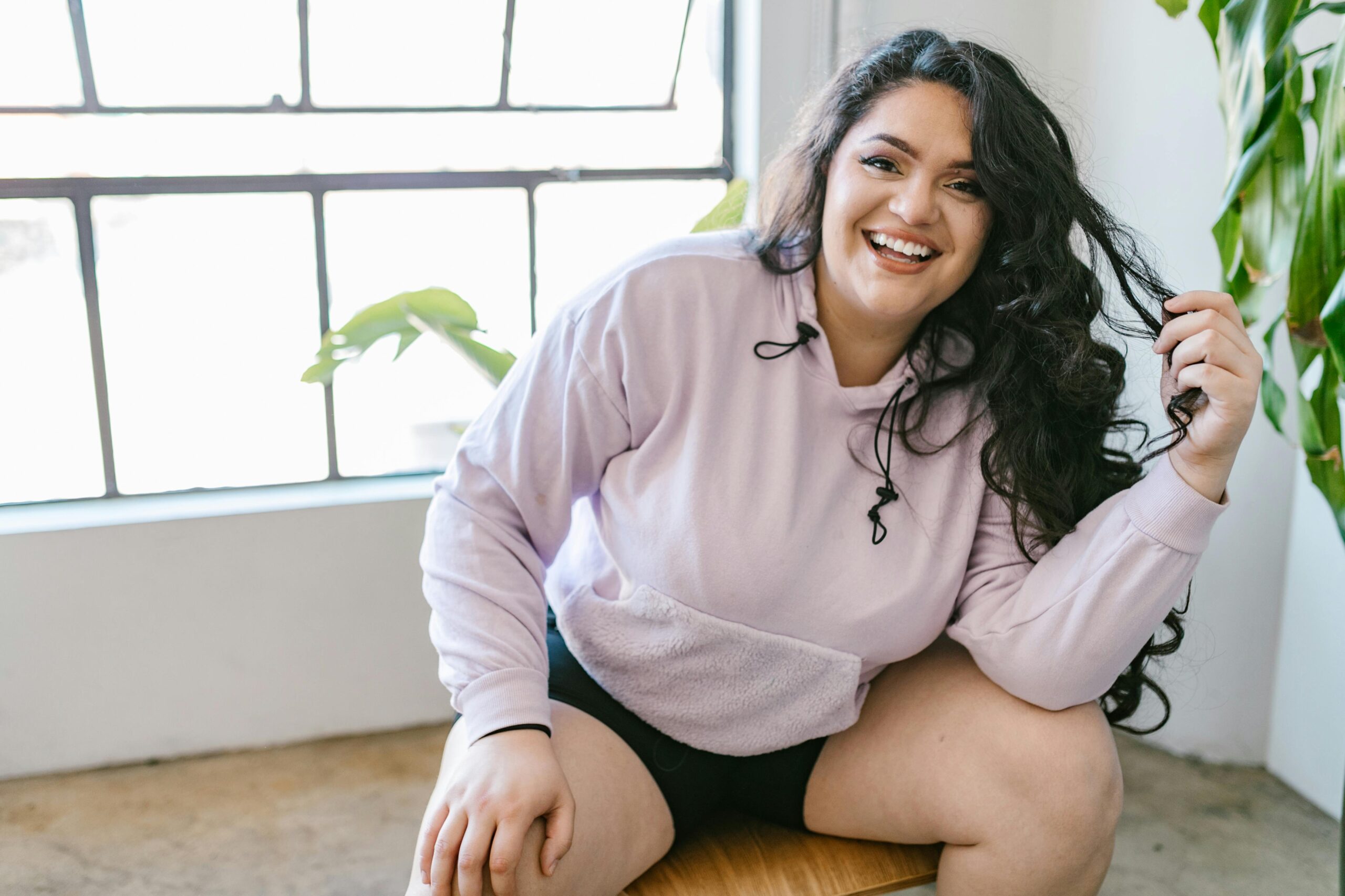 A person sitting on a bench by a window in athleisure wear, smiling.