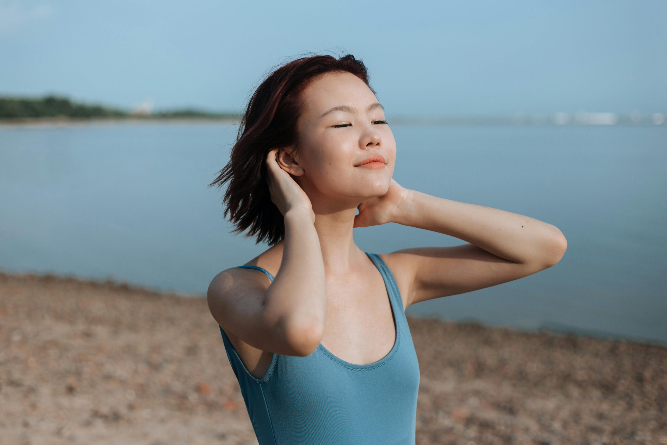 Woman walking on beach with eyes closed, looking content and relaxed.